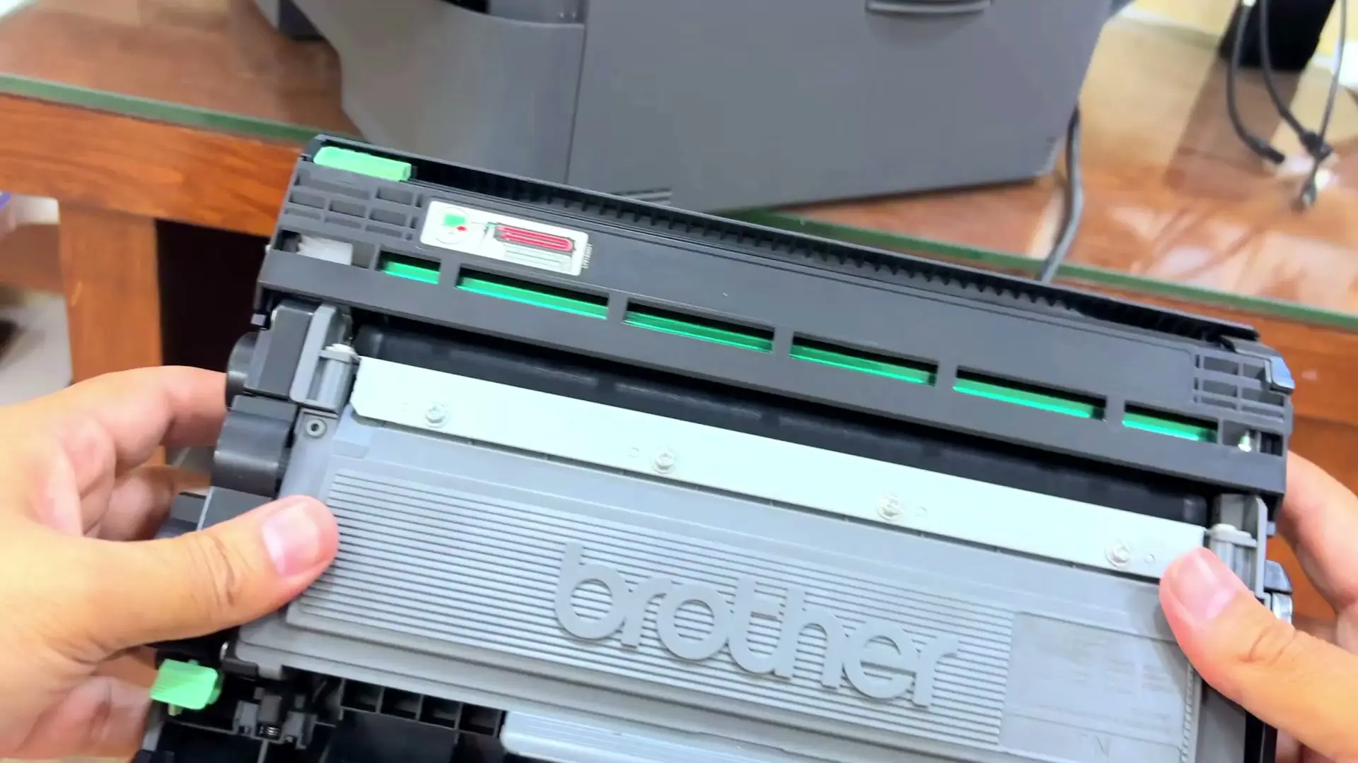 The old Brother toner cartridge seated in the printer's drum unit, held in two hands