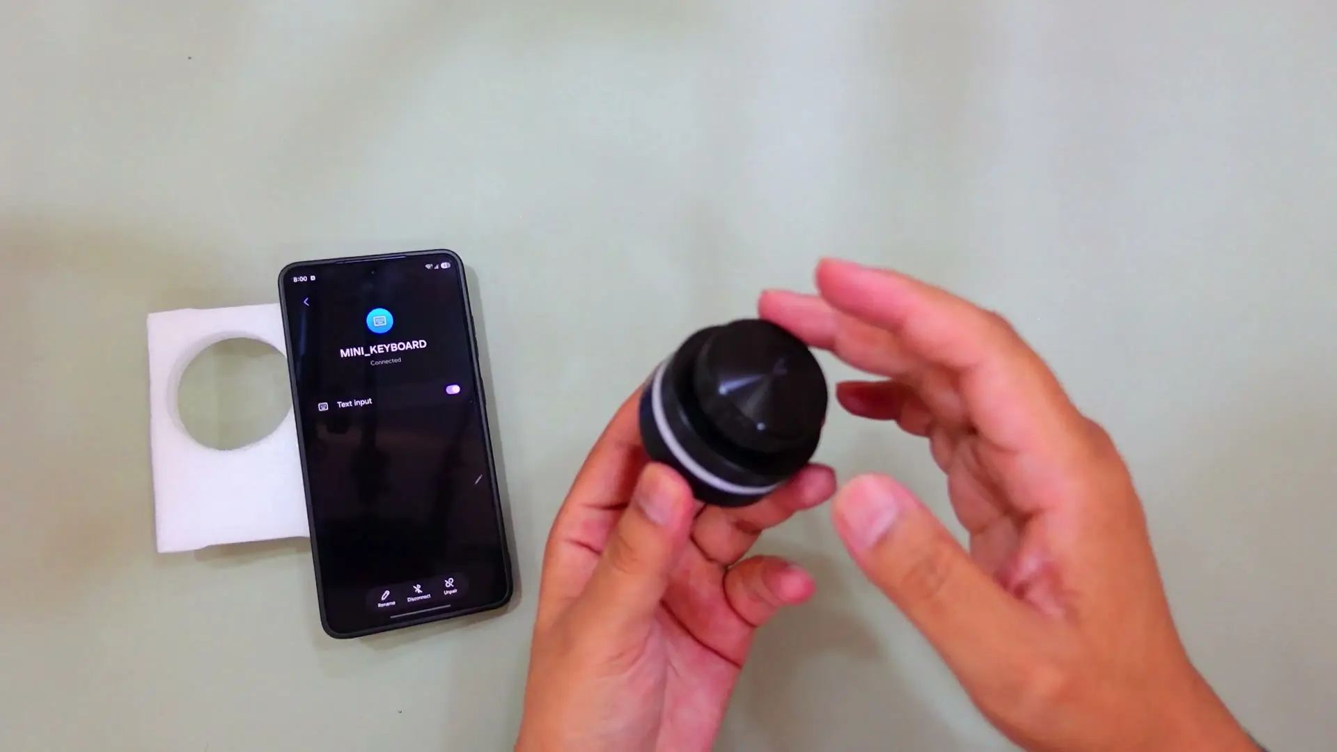 Android phone paired over Bluetooth to the mini keyboard controller while hands rotate the top dial
