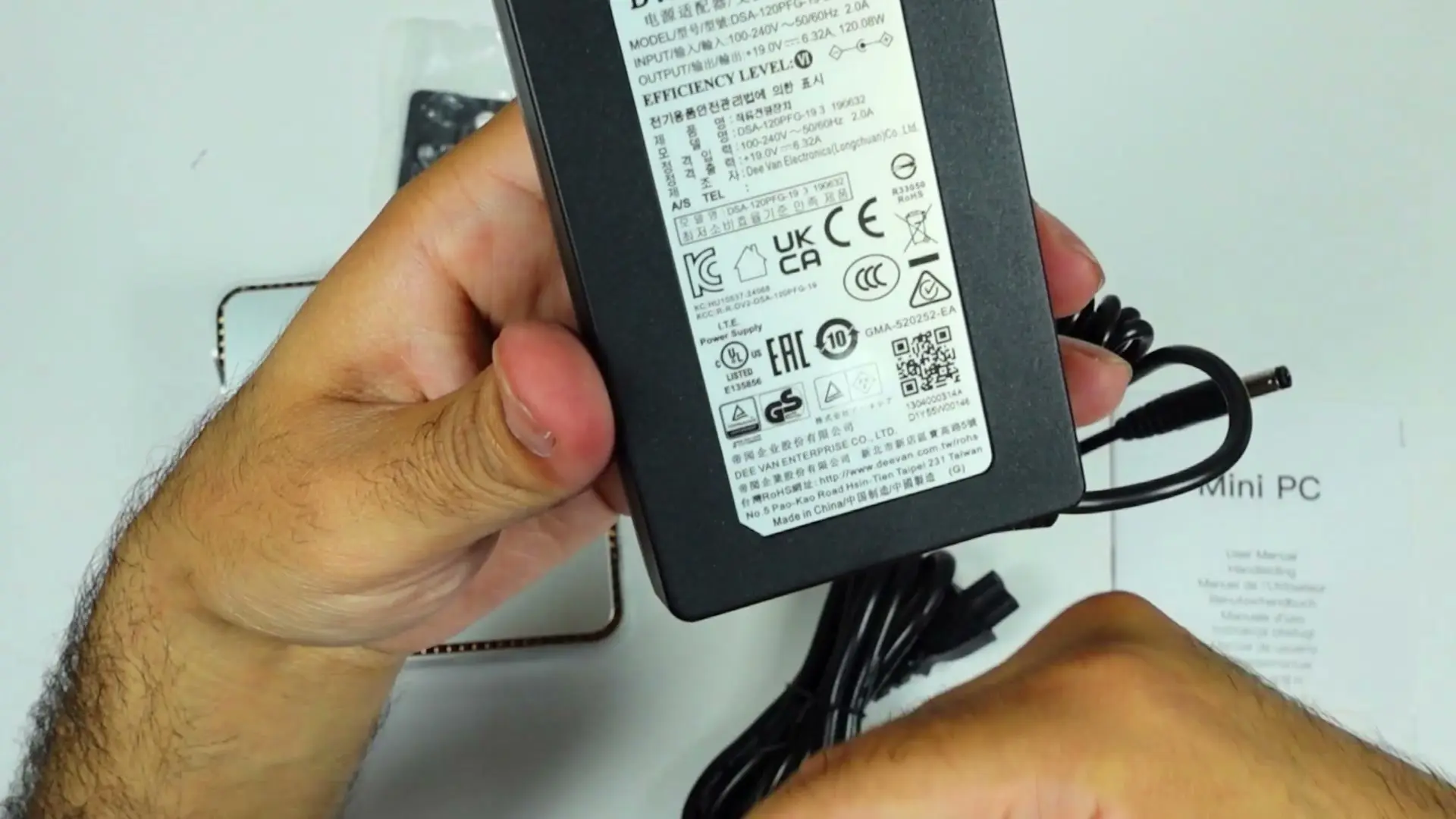 Hands holding the KAMRUI 120W power brick with its rating label visible