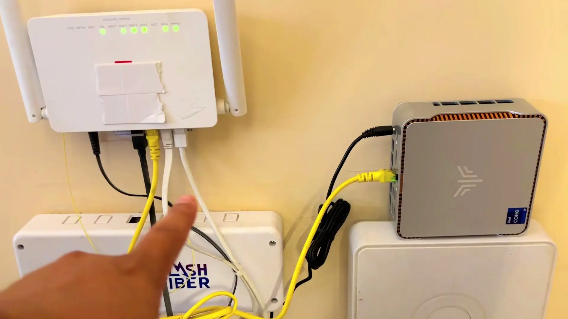 KAMRUI Hyper H2 mini PC on a shelf beside a Wi-Fi router, connected with a yellow Ethernet cable