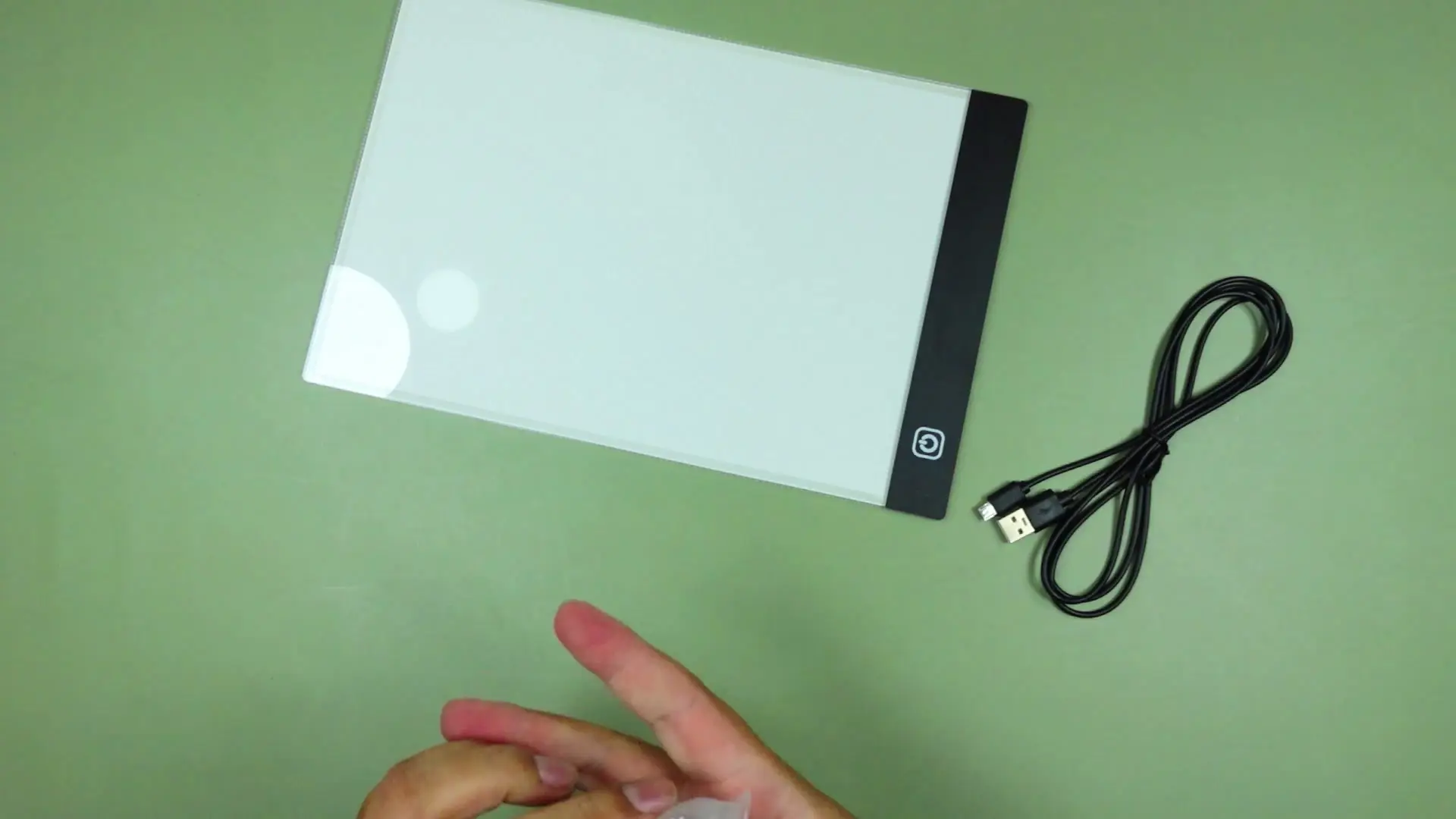 The light pad lying flat on the test desk with its micro-USB charging cable beside it, still partly in its plastic wrapping