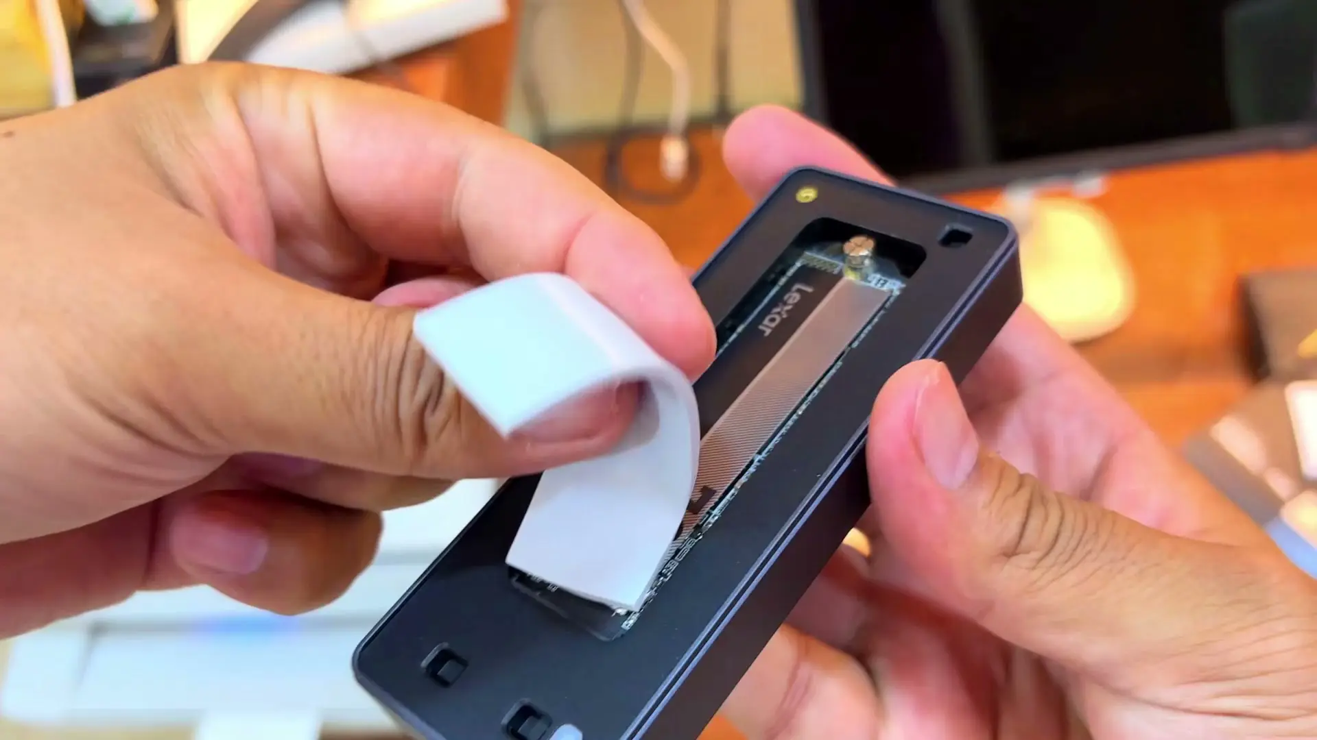 Hands laying the UGREEN enclosure's white silicone thermal pad over the Lexar drive installed in the open enclosure