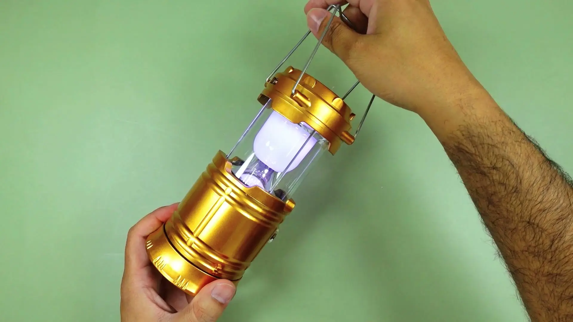 The gold camping lantern fully extended with its carry handle raised and the light lit, showing the telescoping design expanded