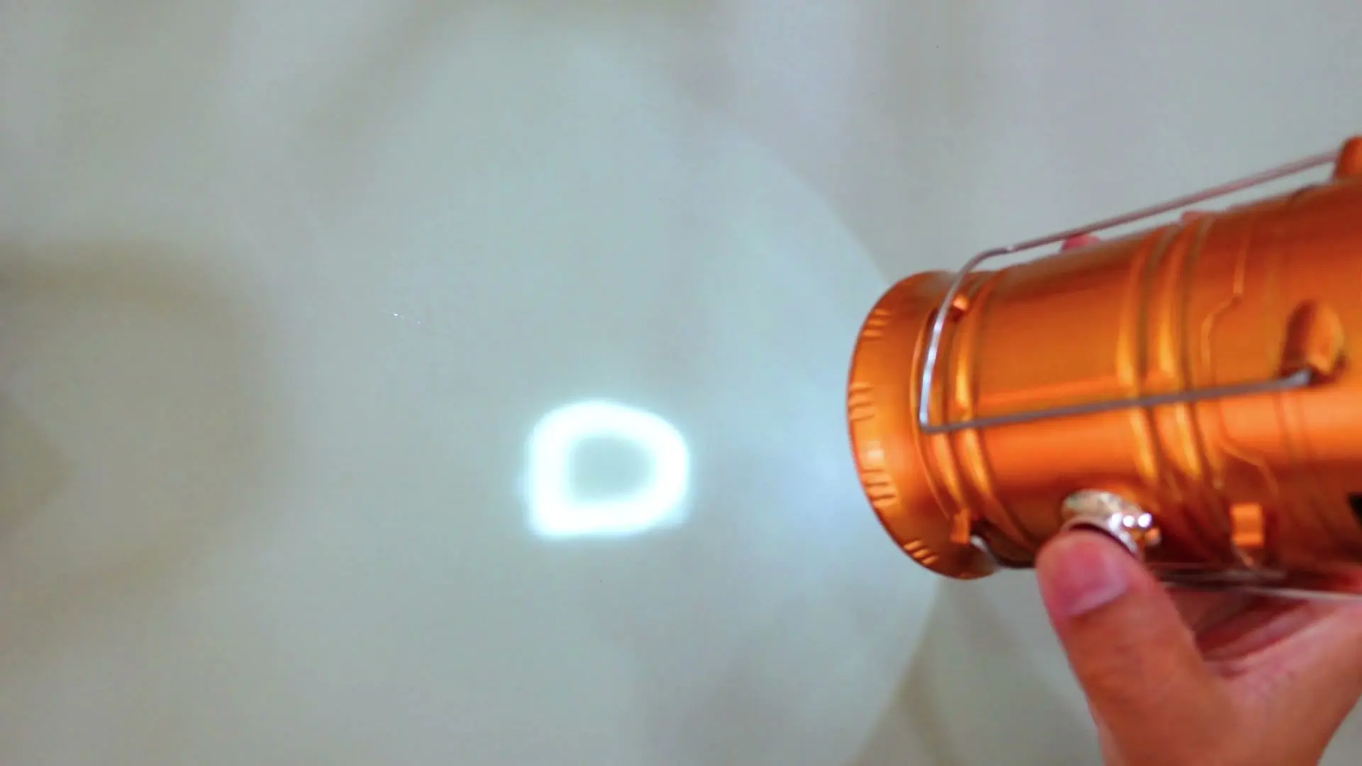 The lantern's flashlight head turned on, projecting a visible white beam onto a wall
