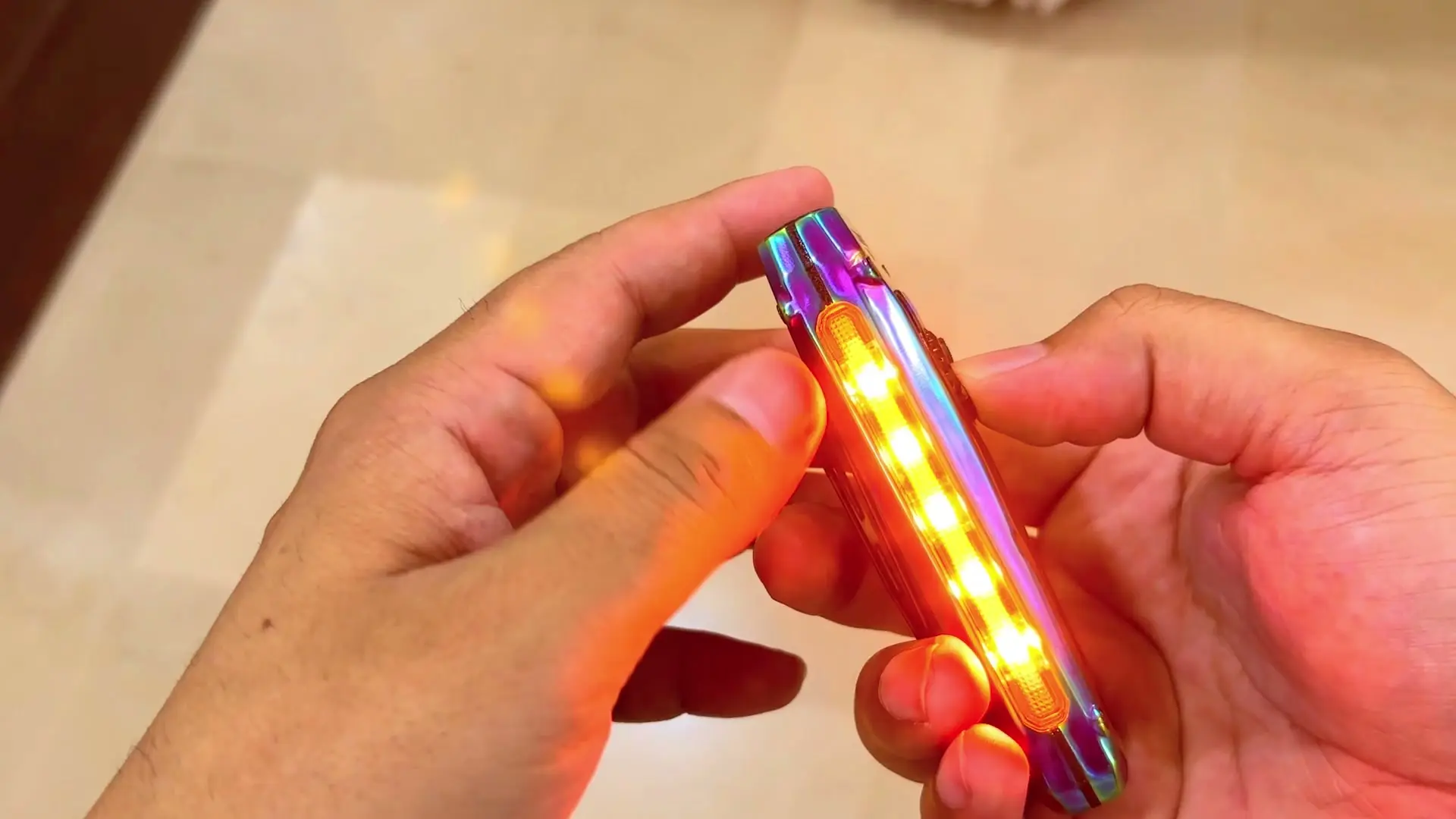 The TUOWEE QL3 held between two hands with the row of LEDs along its edge lit yellow