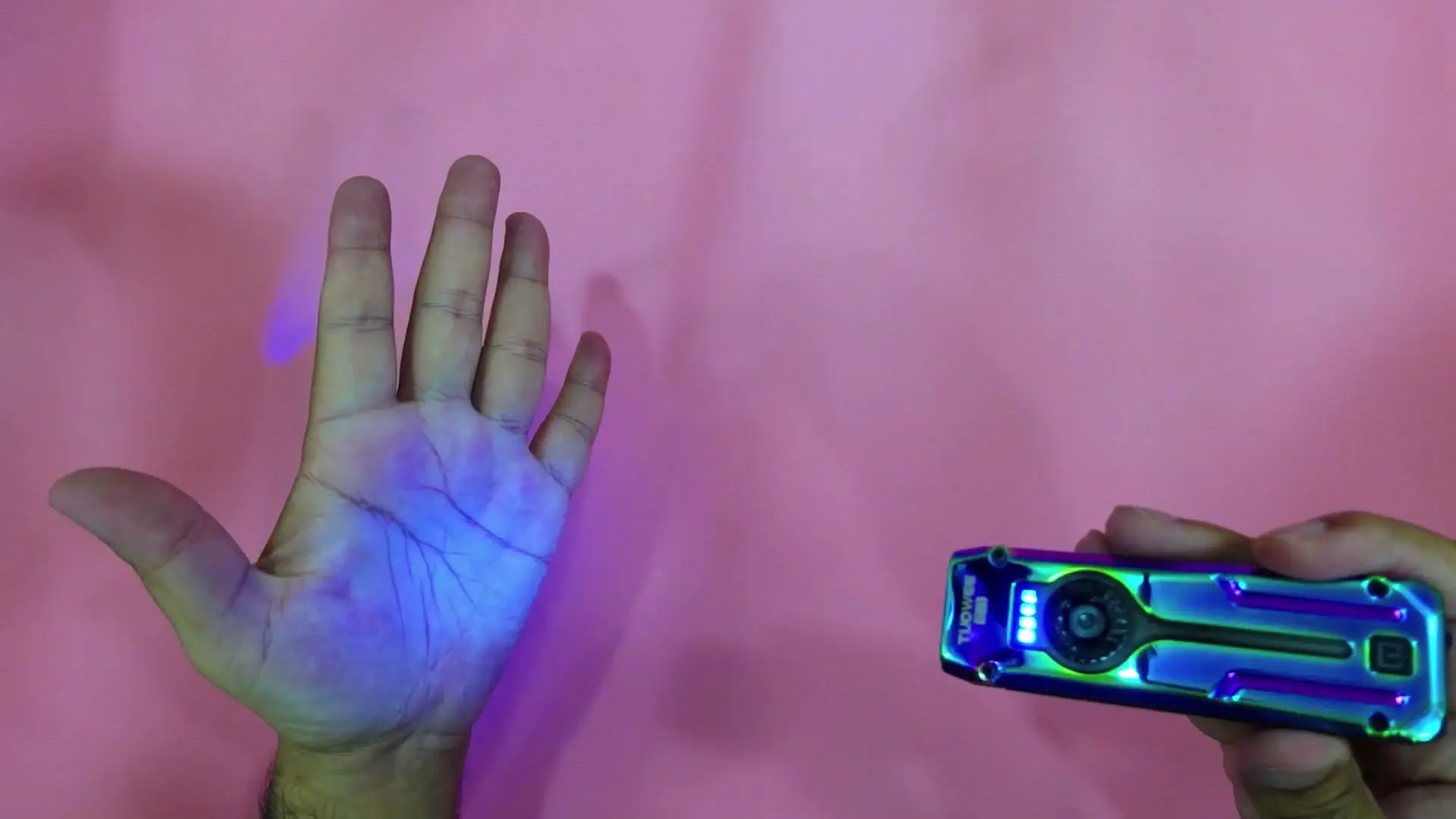 An open palm lit purple by the TUOWEE QL3's UV light on a pink surface