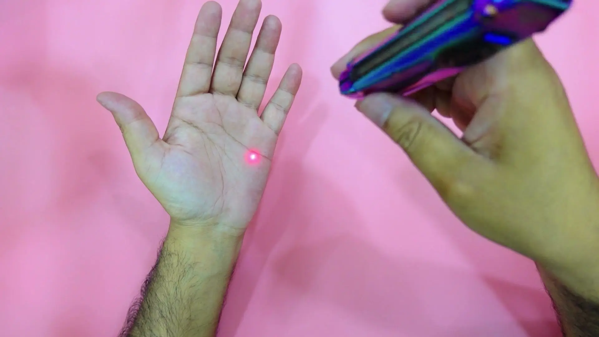 A small red laser dot on an open palm, with the TUOWEE QL3 at the right edge of the frame