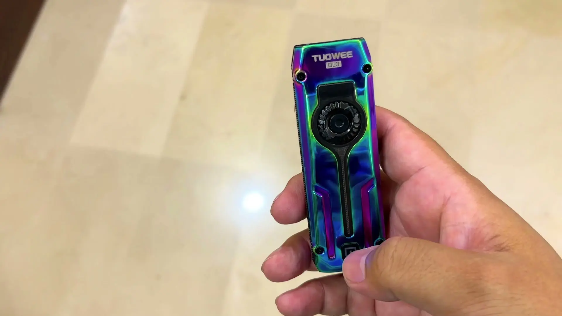 Iridescent blue and purple TUOWEE QL3 EDC flashlight held in hand, showing the TUOWEE logo and the round dial on its face