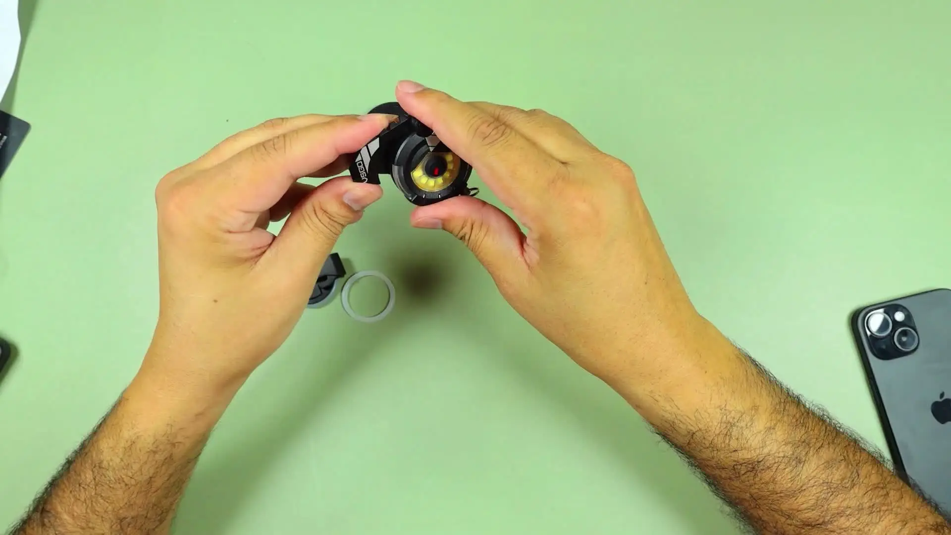VSGO EDC light held in hands with clip mount pieces and a metal ring laid out on the desk beside it