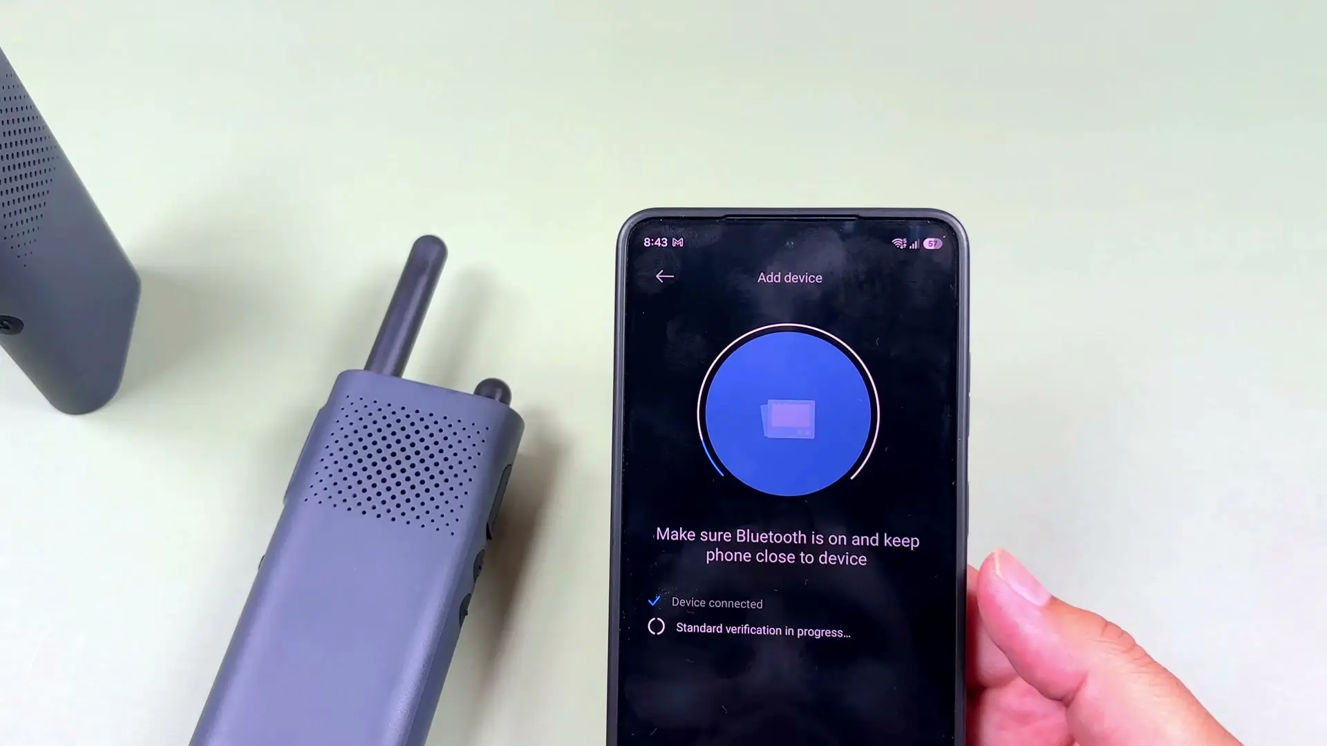 Two Xiaomi walkie talkies on a desk next to a phone showing Mi Home device discovery